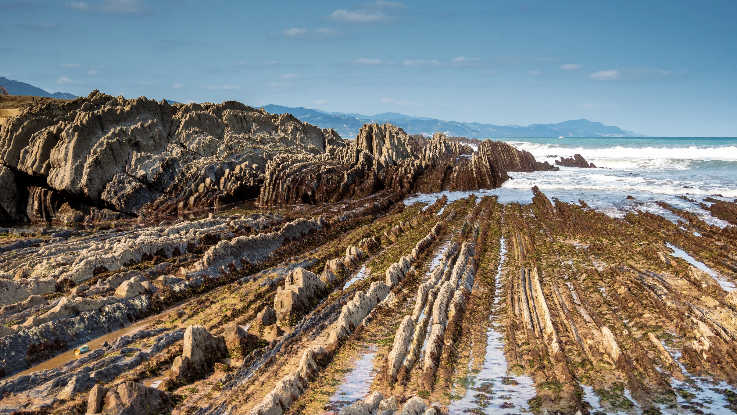 flat, jagged vertical rock formations meet breaking ocean waves