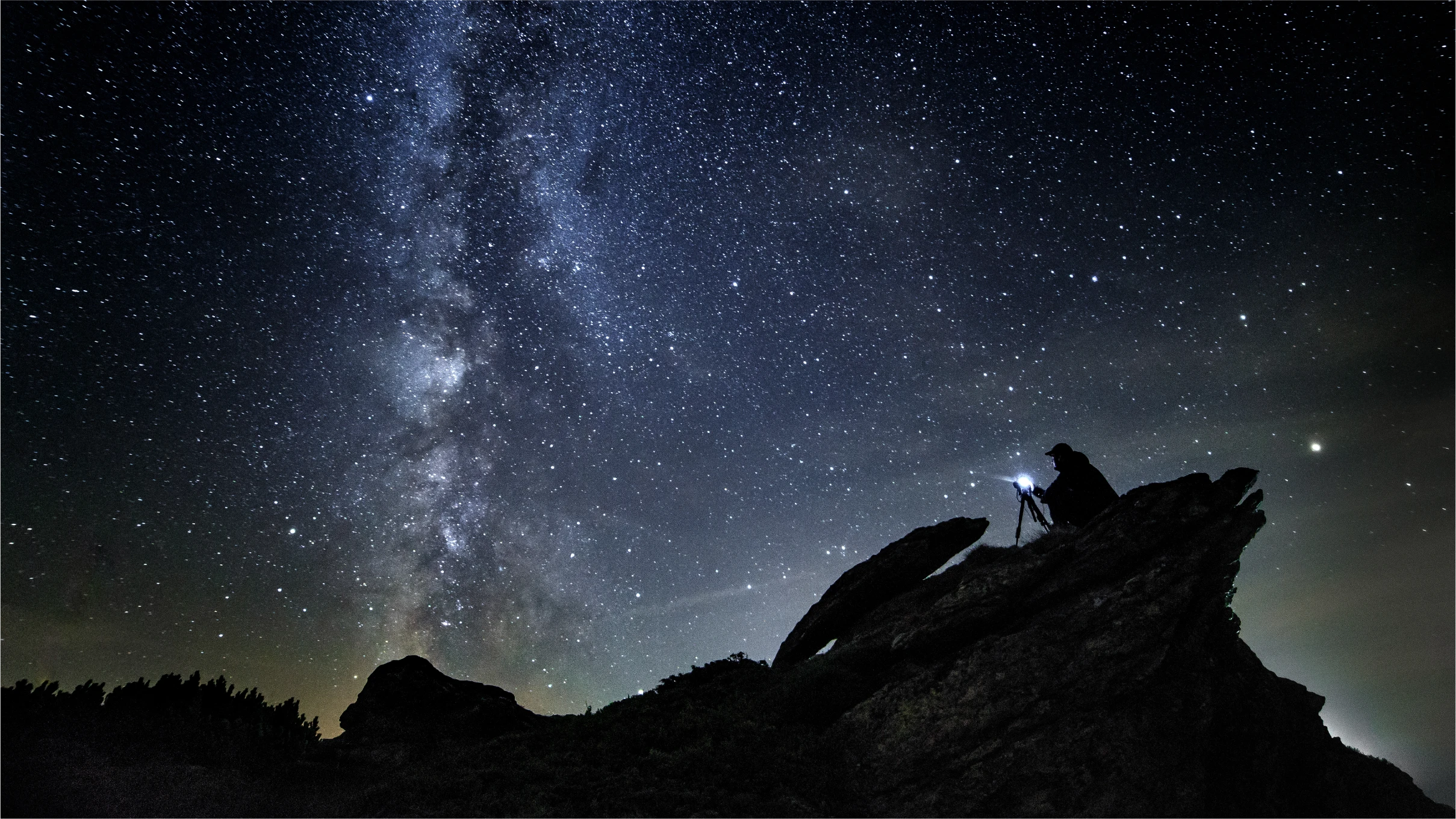 beneath the Milky Way, someone sets up a tripod